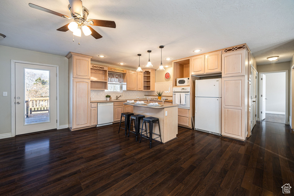 Kitchen with white appliances, a breakfast bar area, a center island, light brown cabinetry, and decorative light fixtures