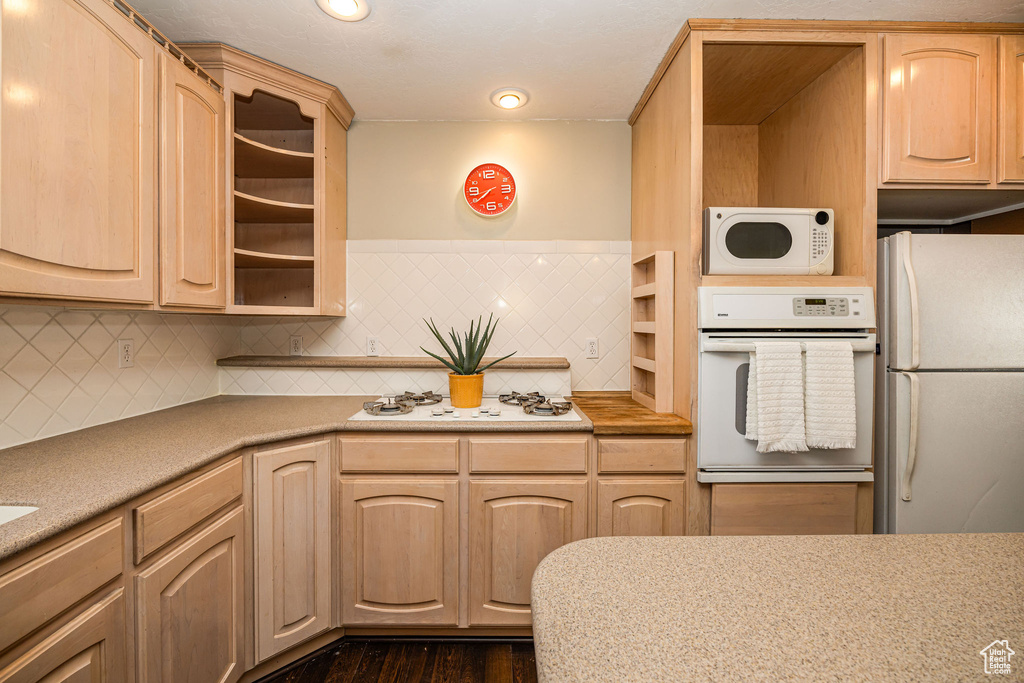 Kitchen with light brown cabinetry, backsplash, and white appliances