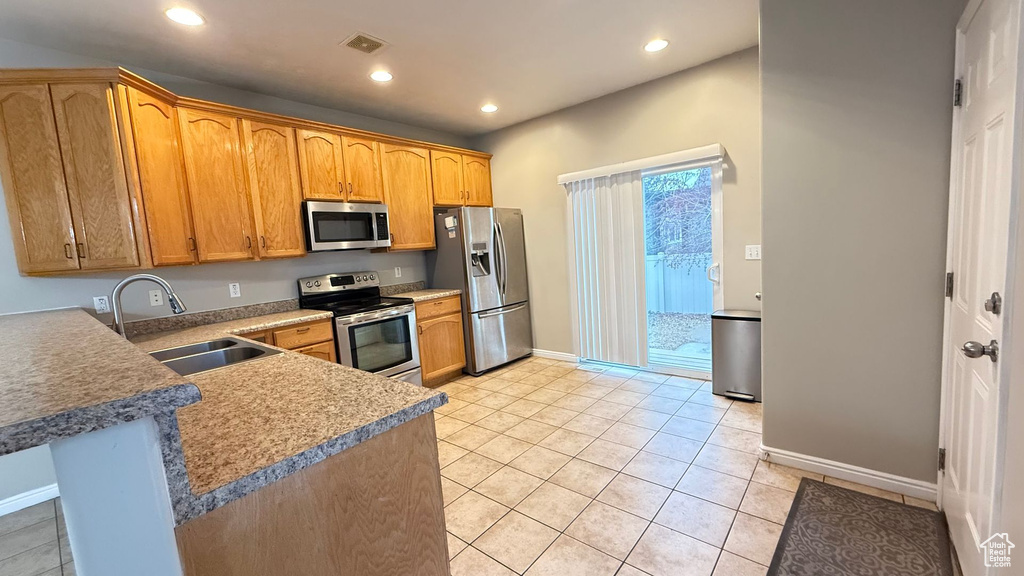 Kitchen featuring sink, light tile patterned floors, kitchen peninsula, and appliances with stainless steel finishes