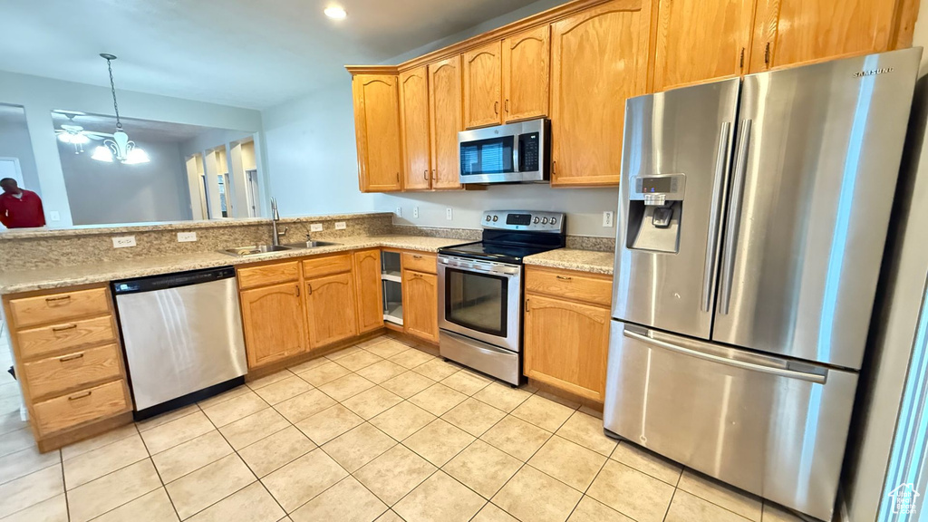 Kitchen featuring sink, appliances with stainless steel finishes, hanging light fixtures, light stone countertops, and light tile patterned flooring