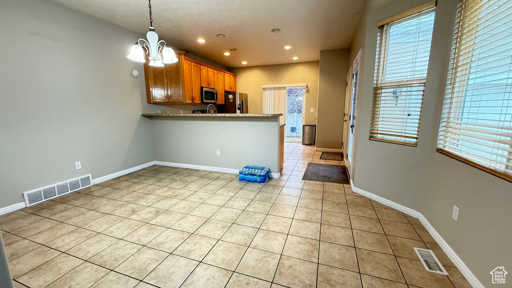 Kitchen with light tile patterned flooring, hanging light fixtures, kitchen peninsula, a notable chandelier, and stainless steel appliances