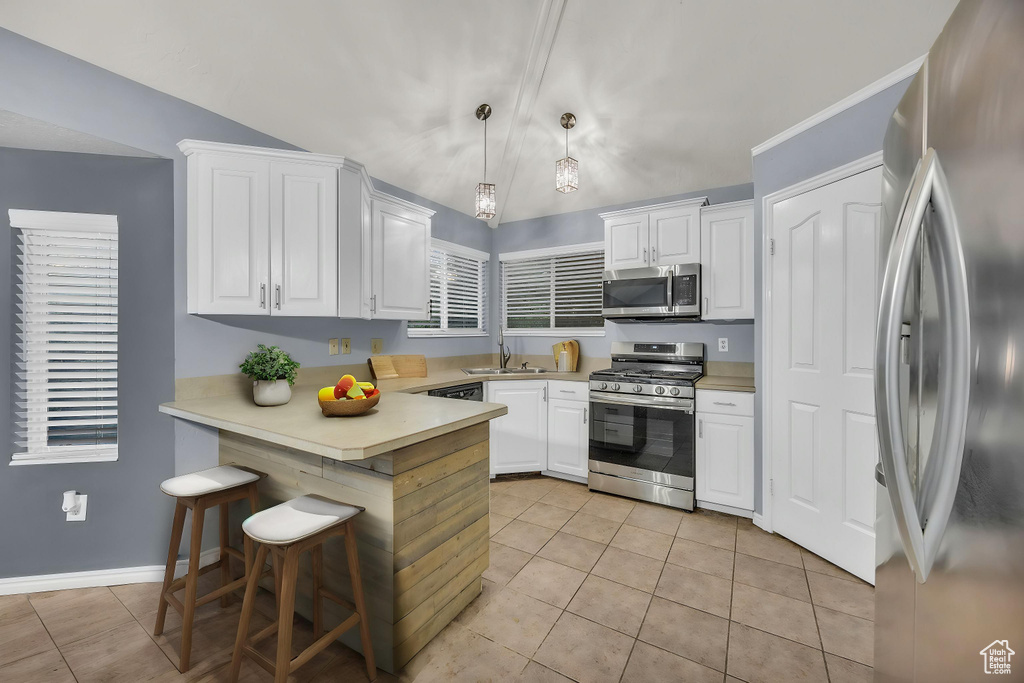 Kitchen with a peninsula, lofted ceiling, light tile patterned flooring, white cabinetry, and appliances with stainless steel finishes