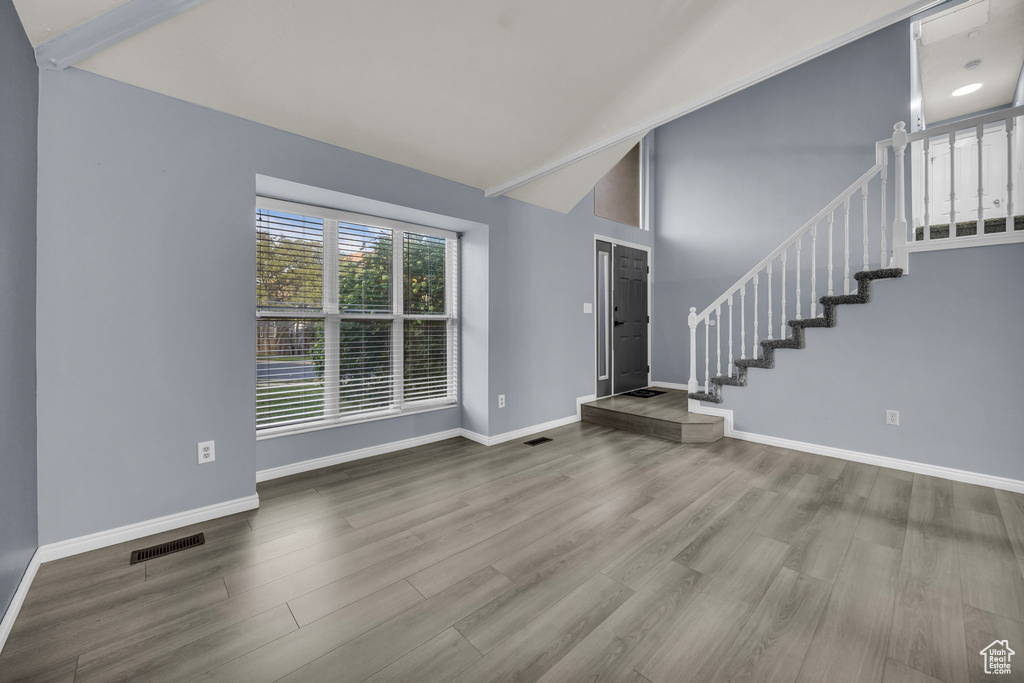 Unfurnished living room with visible vents, wood finished floors, high vaulted ceiling, baseboards, and stairs