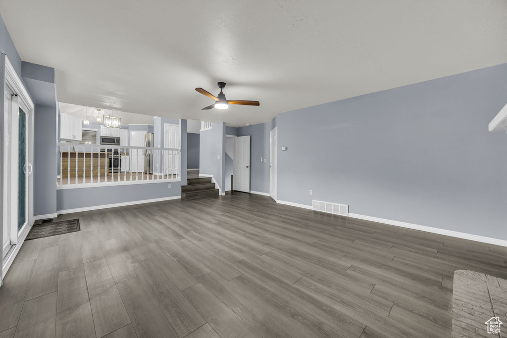 Unfurnished living room with visible vents, dark wood-style flooring, baseboards, stairway, and ceiling fan with notable chandelier