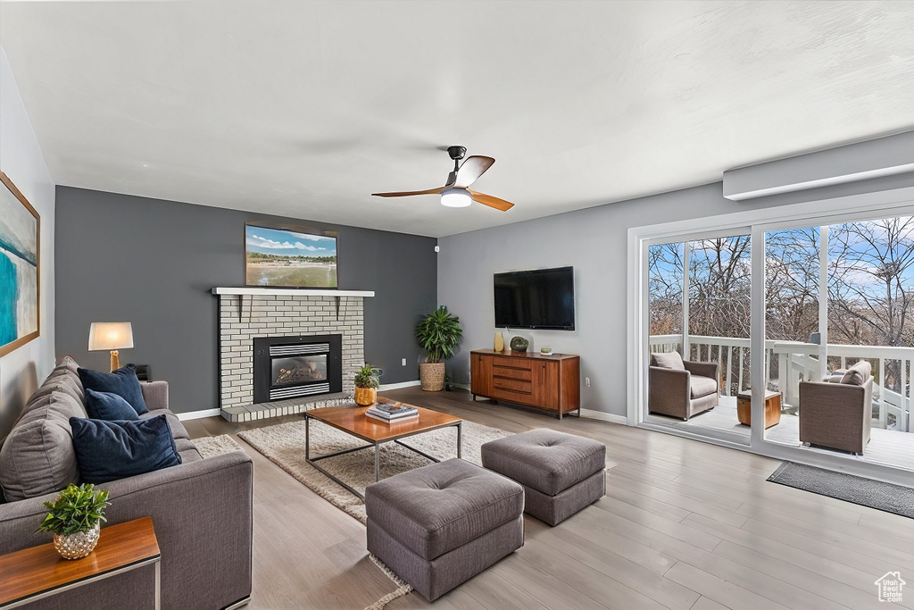 Living area with a brick fireplace, ceiling fan, baseboards, and wood finished floors