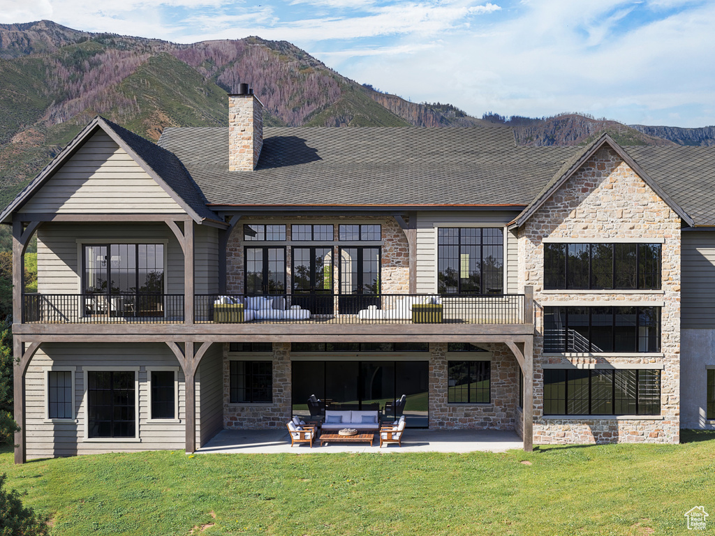 Rear view of property featuring stone siding, a patio area, a lawn, and a mountain view
