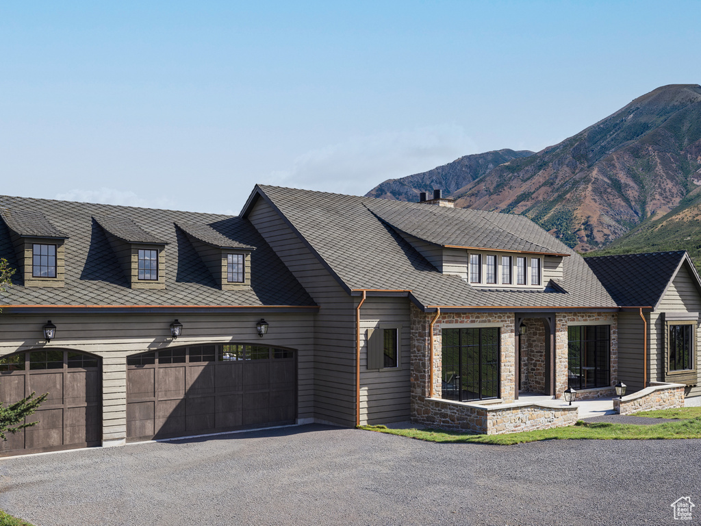 View of front facade with an attached garage, asphalt driveway, stone siding, a mountain view, and a chimney