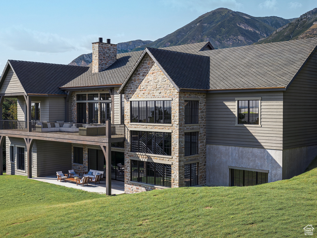 Back of house featuring stone siding, a yard, a patio, a chimney, and a mountain view