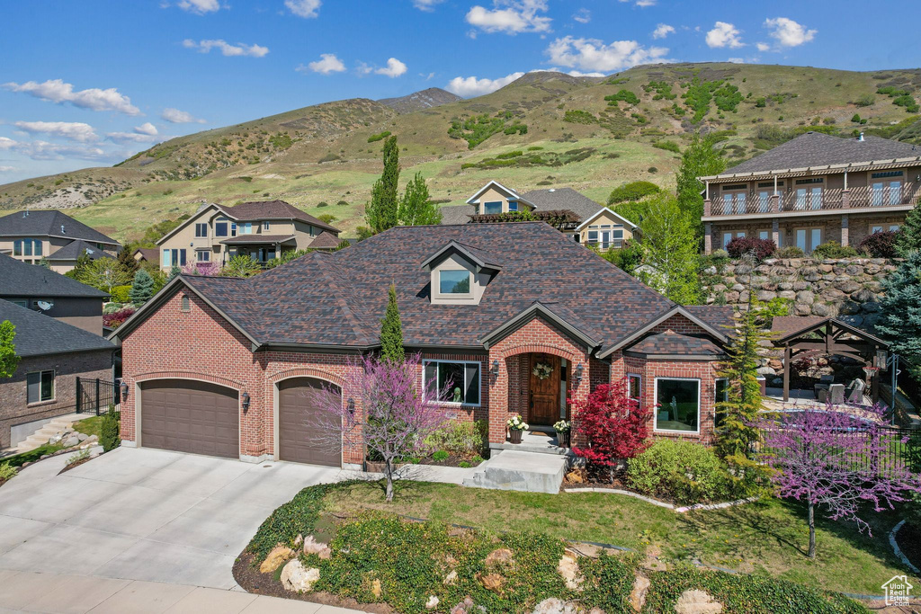 View of front of property featuring a residential view, brick siding, a garage, a mountain view, and concrete driveway