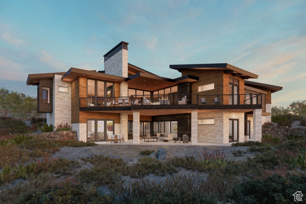 Rear view of house featuring a balcony, stone siding, and a patio area