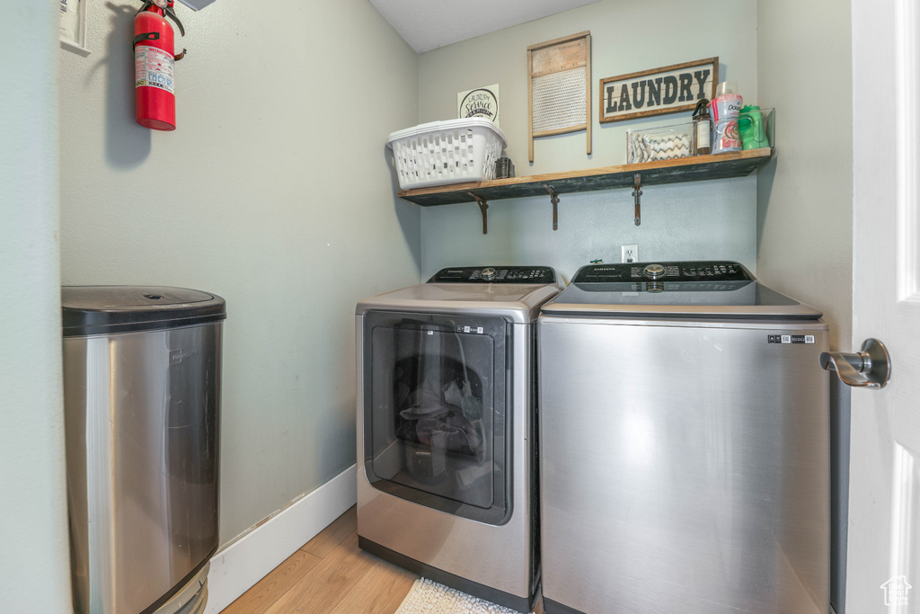Clothes washing area featuring washing machine and dryer, baseboards, light wood finished floors, and laundry area
