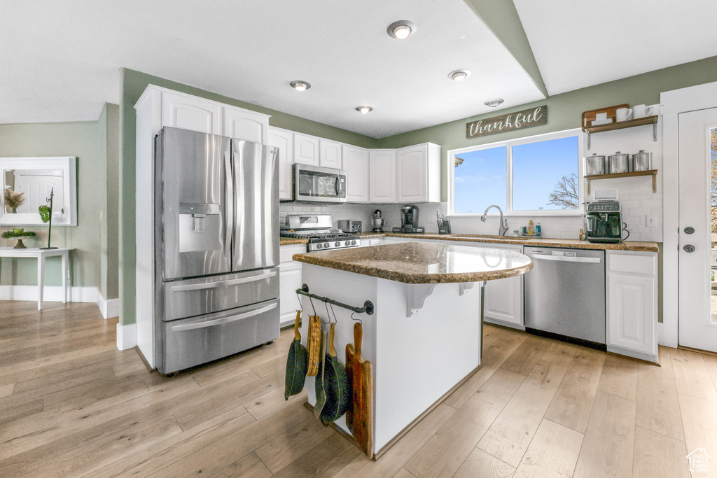 Kitchen with white cabinets, decorative backsplash, dark stone counters, and appliances with stainless steel finishes