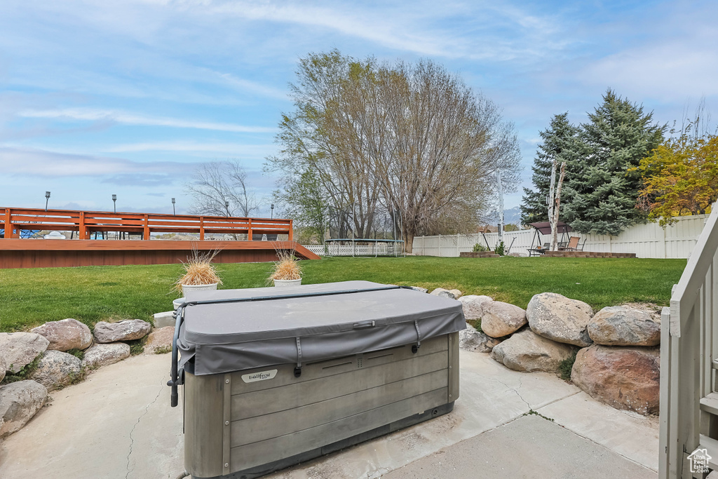 View of patio with a fenced backyard, a hot tub, a deck, and a trampoline