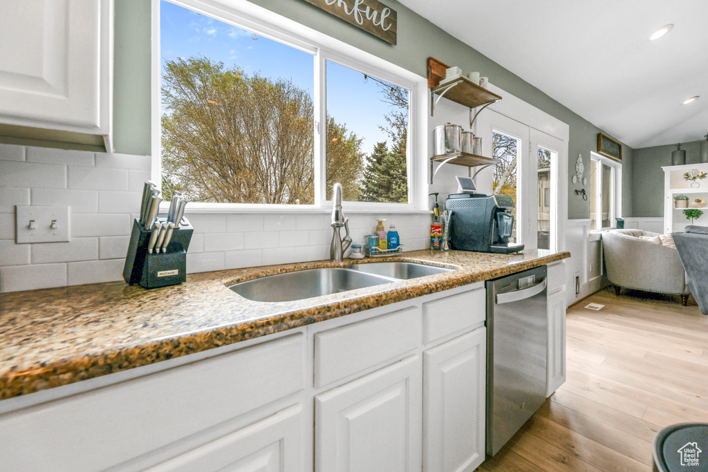 Kitchen featuring white cabinets, a sink, decorative backsplash, light stone counters, and dishwasher