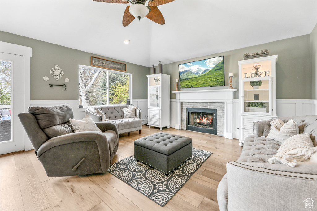 Living area featuring wainscoting, vaulted ceiling, a ceiling fan, wood finished floors, and a fireplace