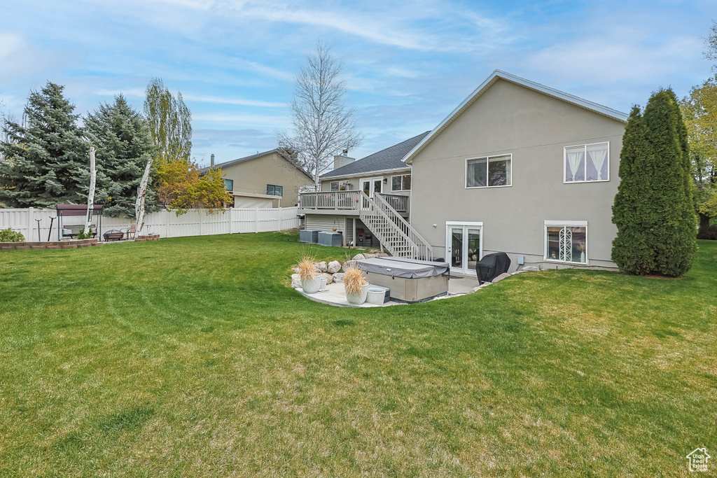 Rear view of property featuring fence, a yard, a wooden deck, french doors, and a hot tub
