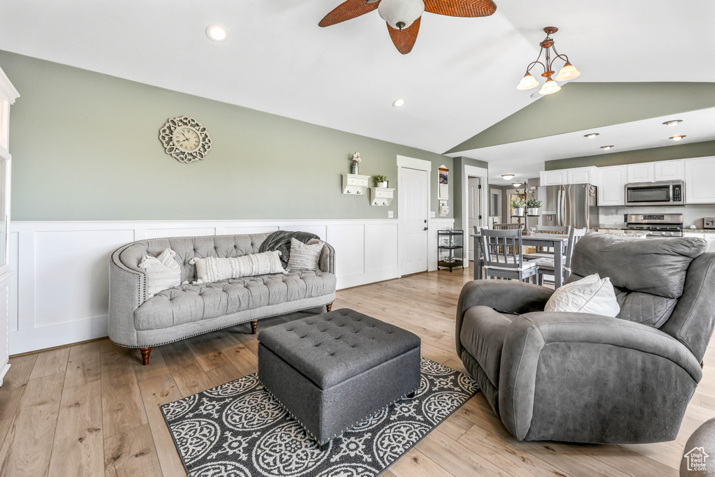 Living room featuring wainscoting, vaulted ceiling, light wood-style floors, and ceiling fan