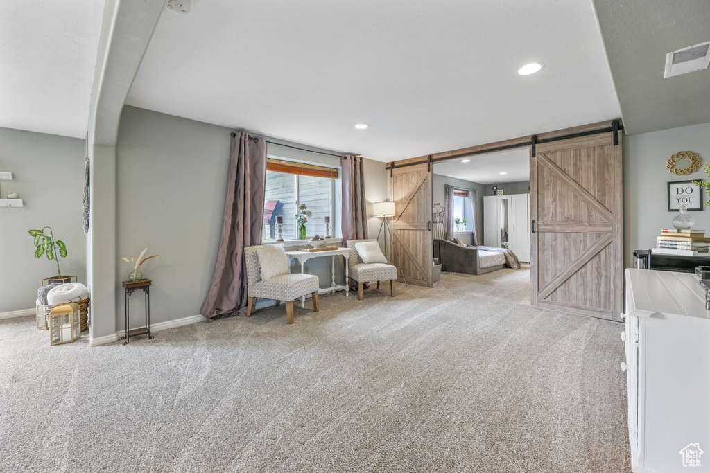 Living area featuring carpet flooring, a barn door, visible vents, baseboards, and recessed lighting