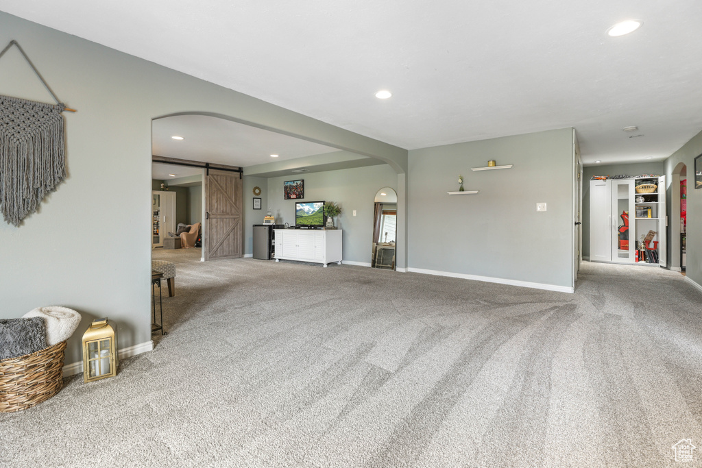 Unfurnished living room with a barn door, arched walkways, carpet flooring, and baseboards