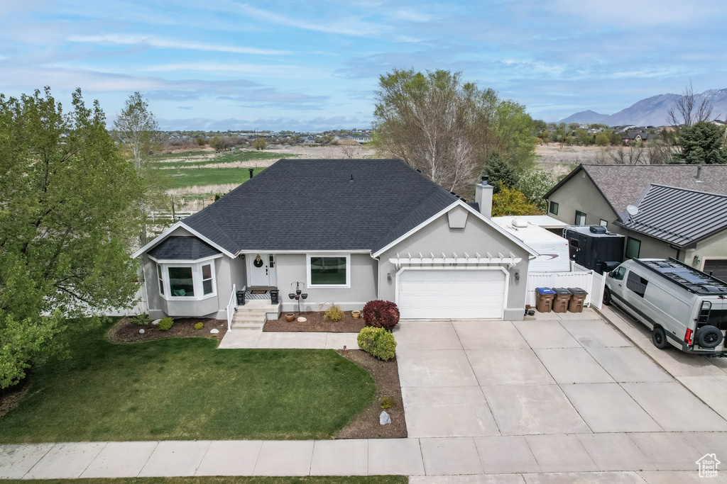 Single story home featuring a shingled roof, a front lawn, an attached garage, driveway, and a mountain view