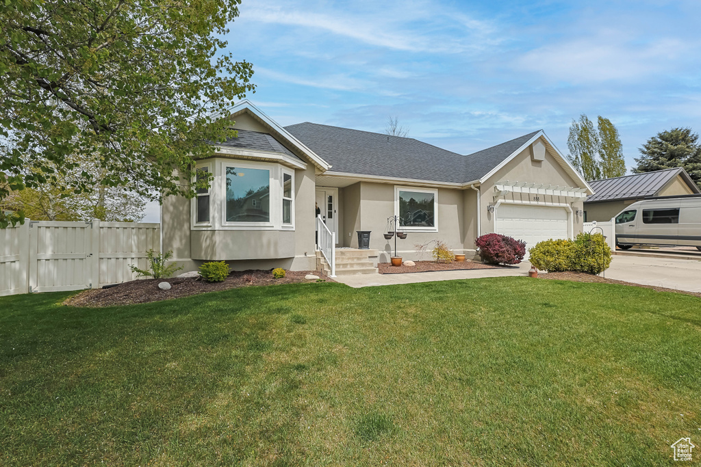 Ranch-style house with an attached garage, fence, driveway, and a front lawn