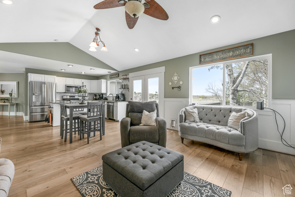 Living area with a wainscoted wall, light wood-style floors, vaulted ceiling, and a ceiling fan