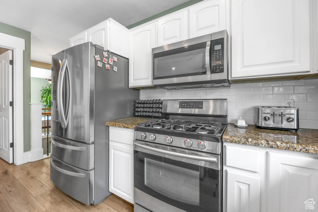 Kitchen with tasteful backsplash, stainless steel appliances, white cabinetry, and light wood-type flooring