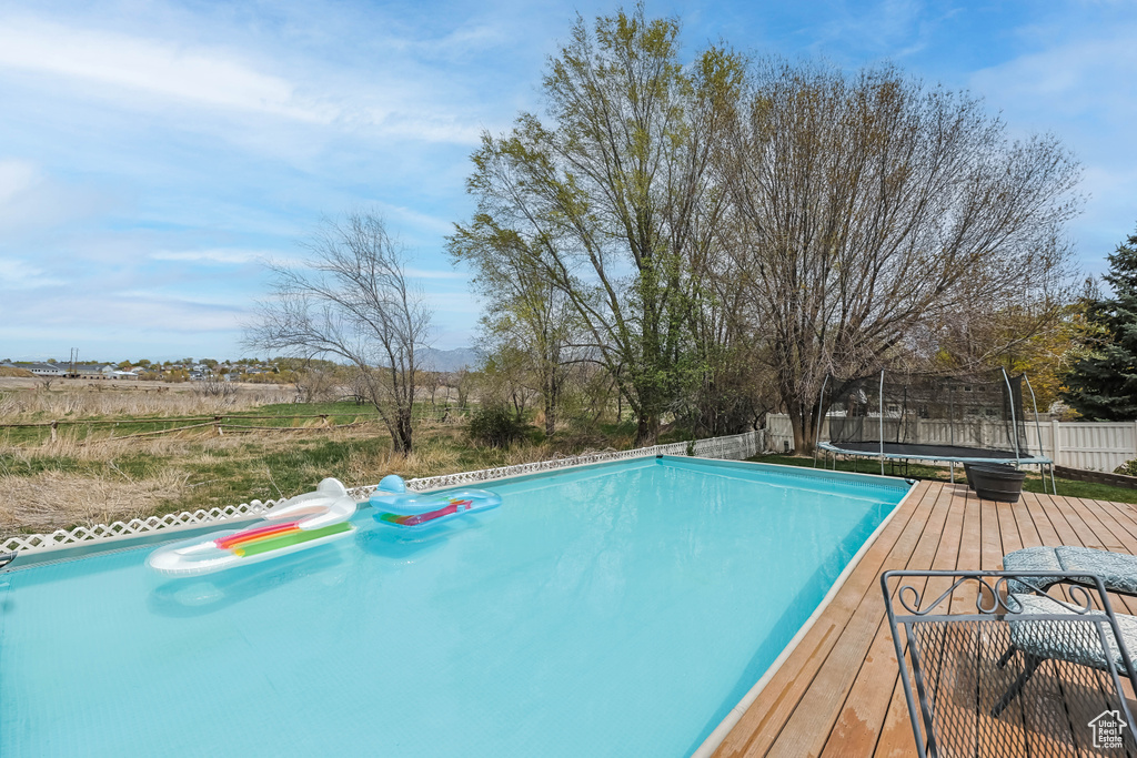 View of swimming pool with fence, a deck, and a trampoline