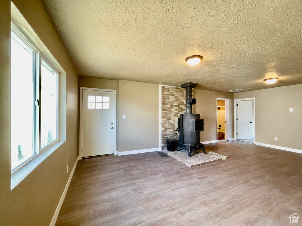 Unfurnished living room featuring light hardwood / wood-style flooring, a textured ceiling, and a wood stove