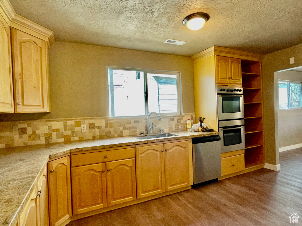 Kitchen with appliances with stainless steel finishes, tasteful backsplash, sink, light hardwood / wood-style floors, and a textured ceiling