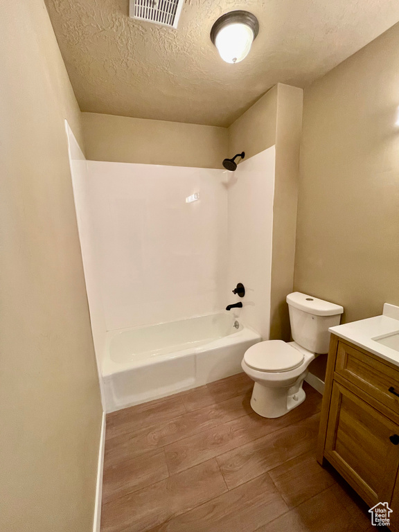 Full bathroom with toilet, wood-type flooring, a textured ceiling, shower / bathtub combination, and vanity