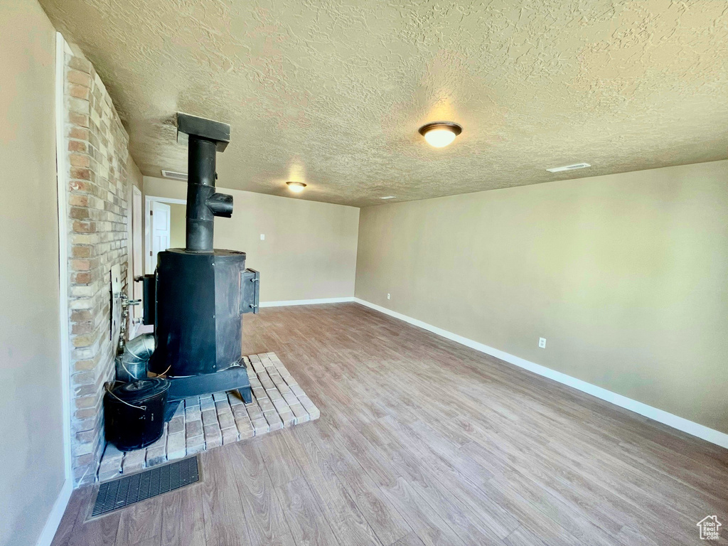 Basement with hardwood / wood-style flooring, a textured ceiling, and a wood stove