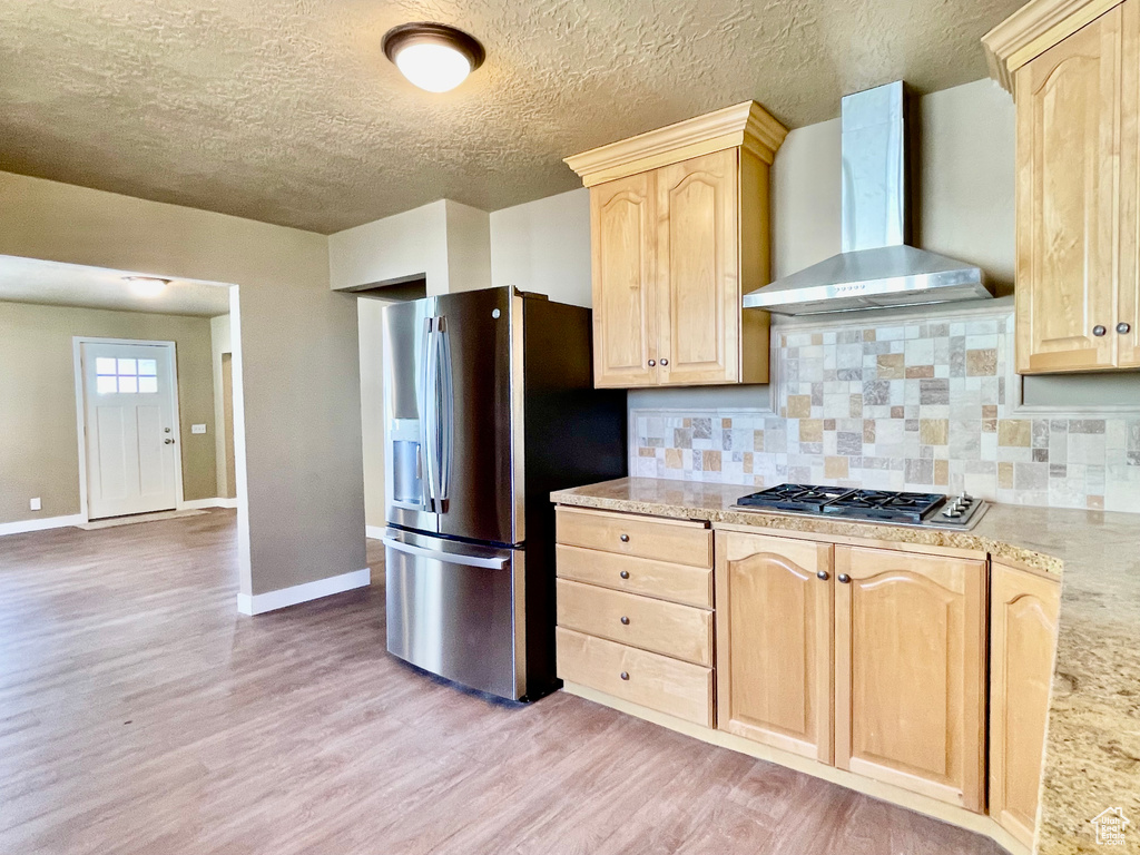 Kitchen with stainless steel appliances, light hardwood / wood-style flooring, light brown cabinetry, and wall chimney exhaust hood