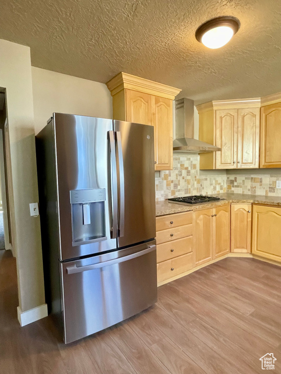 Kitchen featuring appliances with stainless steel finishes, light brown cabinetry, decorative backsplash, wall chimney exhaust hood, and light wood-type flooring