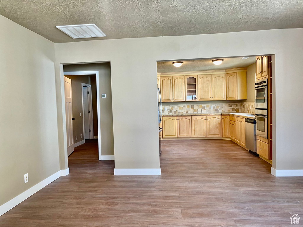 Kitchen with light hardwood / wood-style flooring, stainless steel appliances, tasteful backsplash, a textured ceiling, and light brown cabinets