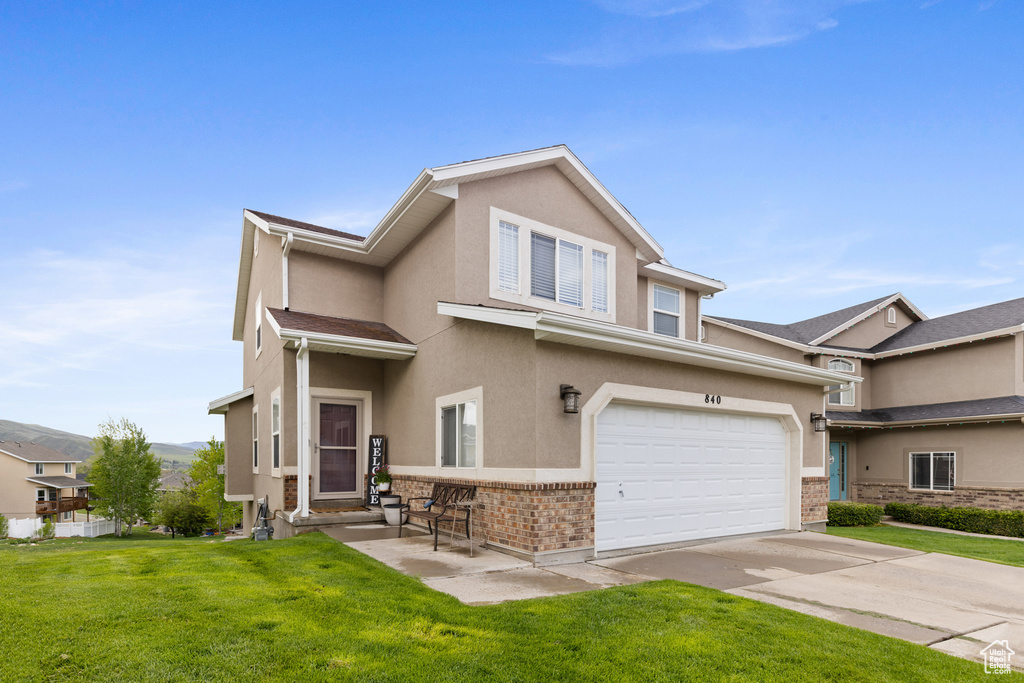 Townhome / multi-family property with brick siding, stucco siding, a front yard, driveway, and a garage