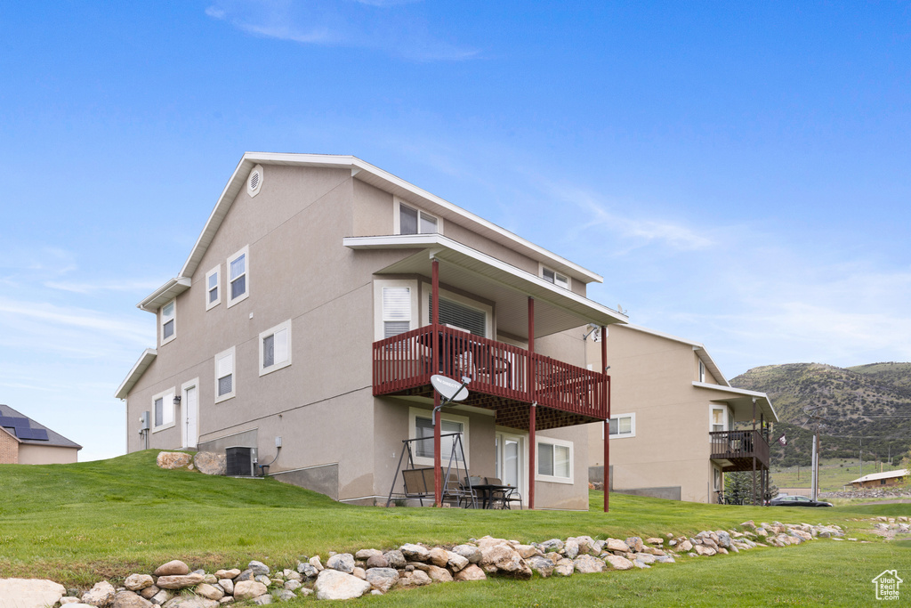 Back of property featuring a yard, central air condition unit, a deck with mountain view, and stucco siding