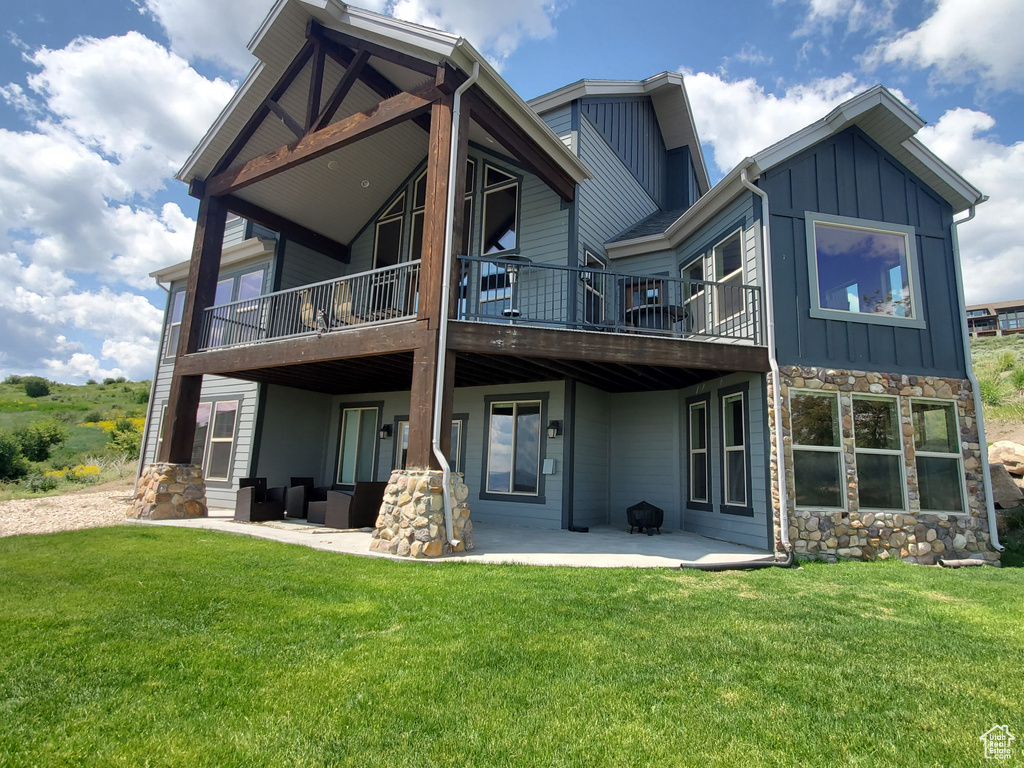 Back of house with board and batten siding, stone siding, a patio, and a yard