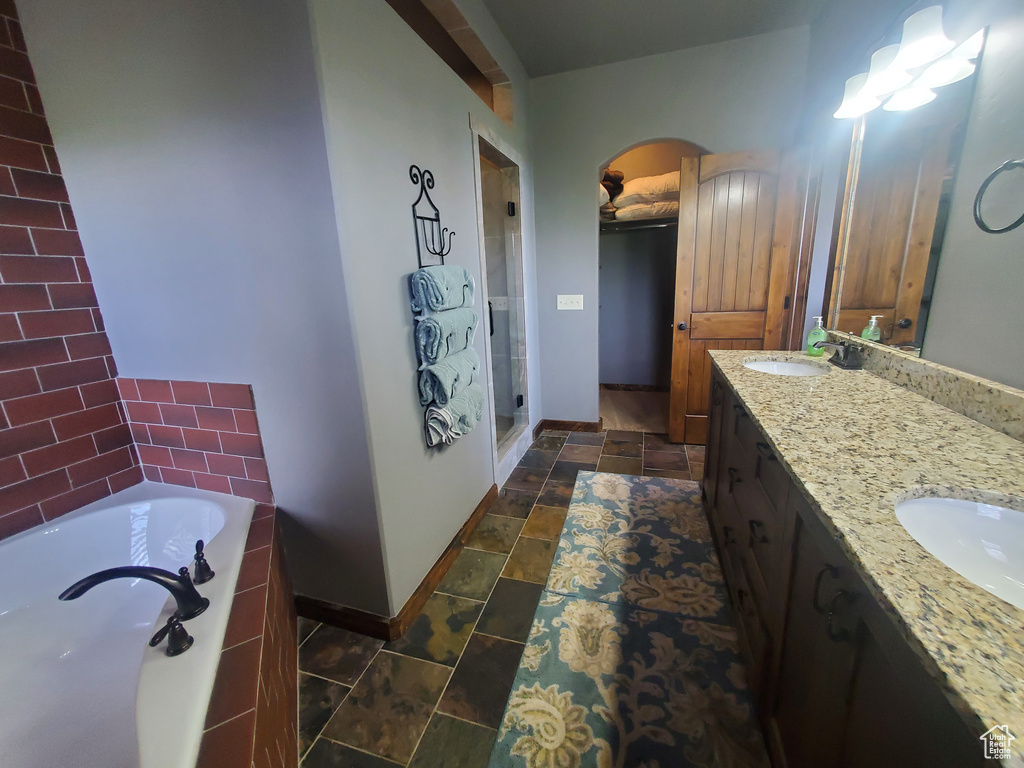 Bathroom featuring baseboards, double vanity, a bath, a stall shower, and stone finish flooring
