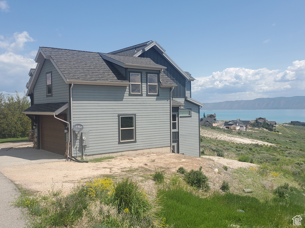 View of property exterior featuring a garage, driveway, a water view, and a shingled roof