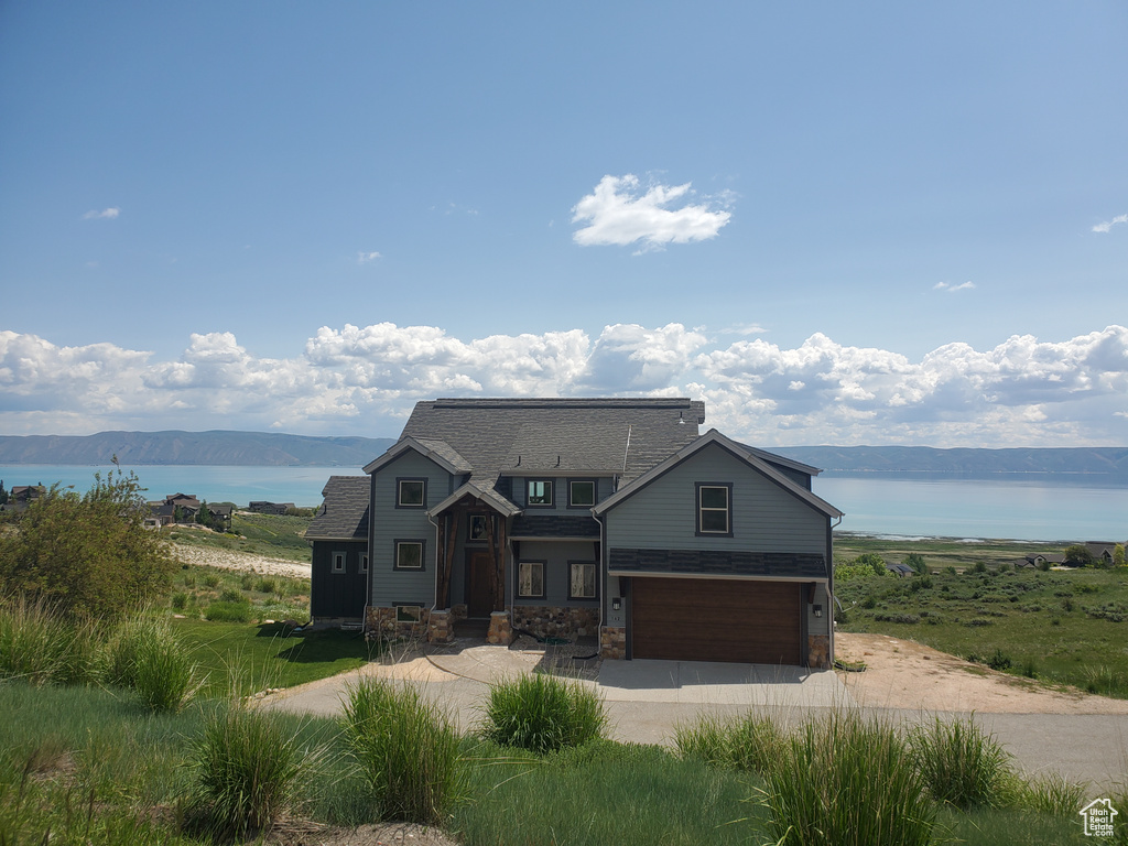 View of front of house with a water view, driveway, an attached garage, and stone siding
