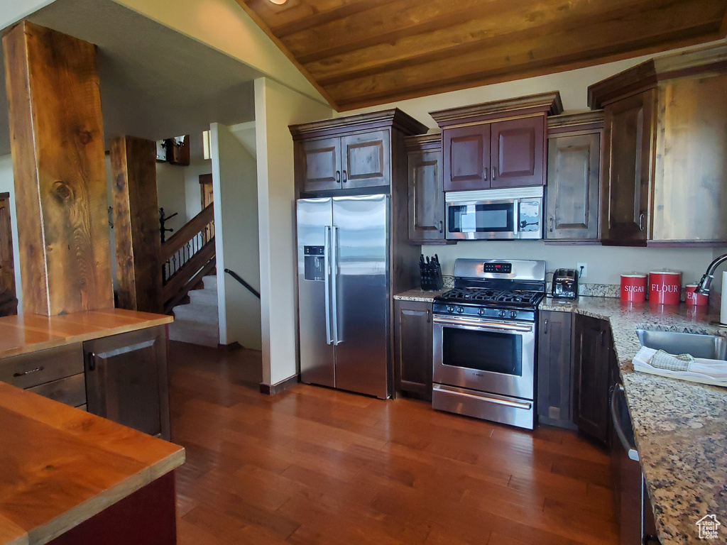 Kitchen with stainless steel appliances, a sink, dark wood-style floors, lofted ceiling, and light stone counters