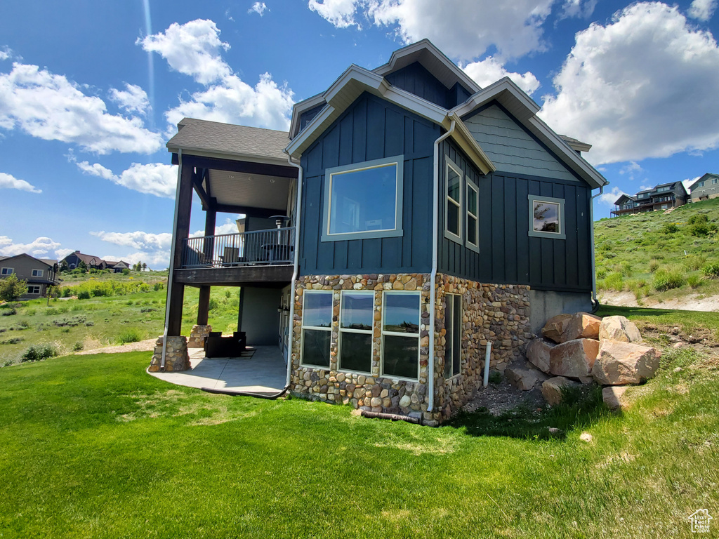 Rear view of property with board and batten siding, stone siding, a patio area, a yard, and a balcony