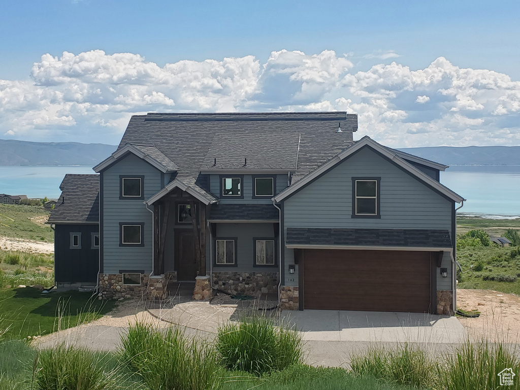 View of front of home featuring a water view, a garage, driveway, and stone siding