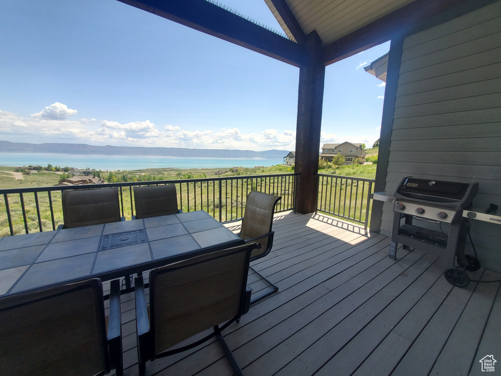 Wooden terrace with a water view, outdoor dining area, and grilling area