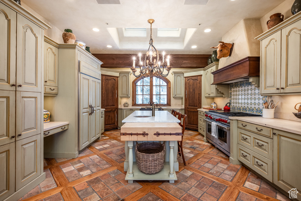 Kitchen with cream cabinetry, a skylight, light countertops, a notable chandelier, and range with two ovens