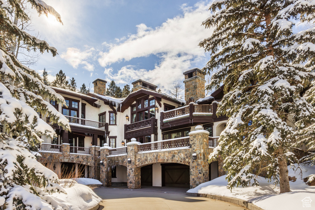 Snow covered rear of property featuring driveway, stone siding, and a garage