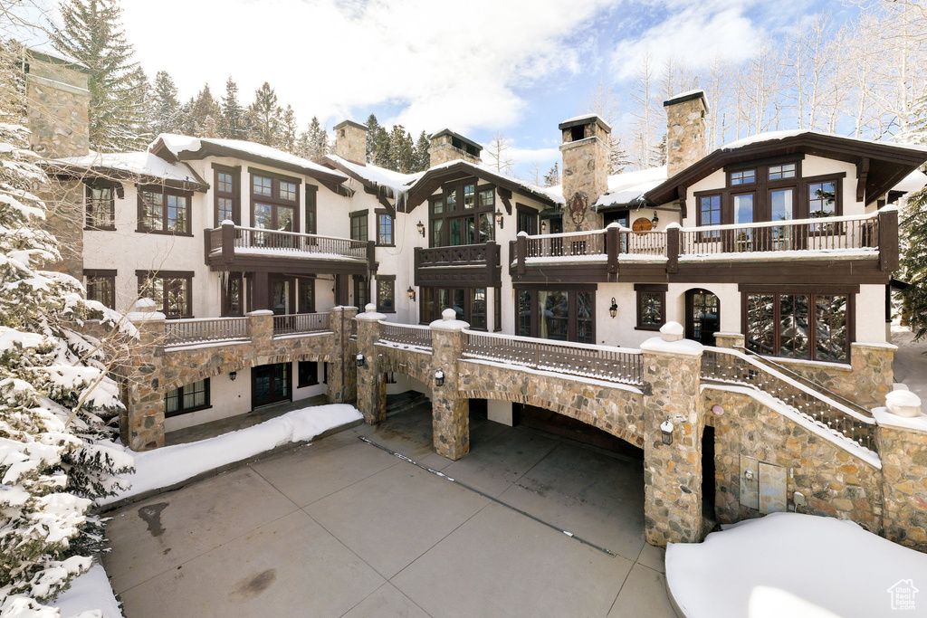 Snow covered house featuring a chimney, a balcony, and stone siding