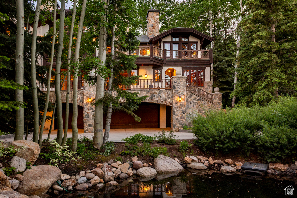 View of front of home featuring a balcony, stairs, a chimney, and stone siding