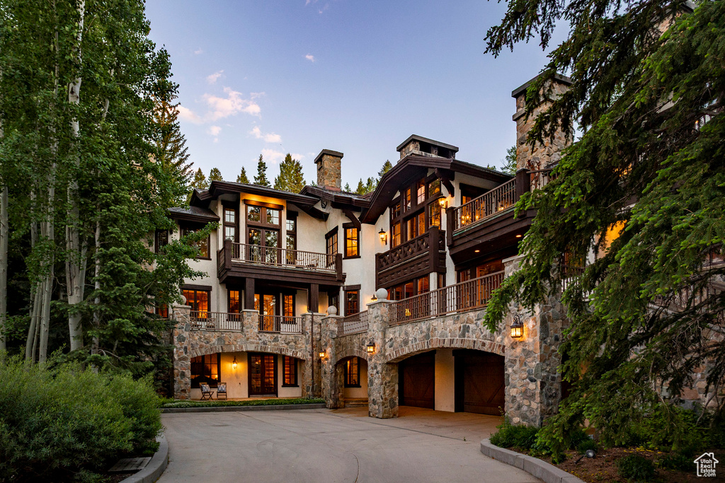 View of front of house featuring curved driveway, stone siding, a chimney, and stucco siding